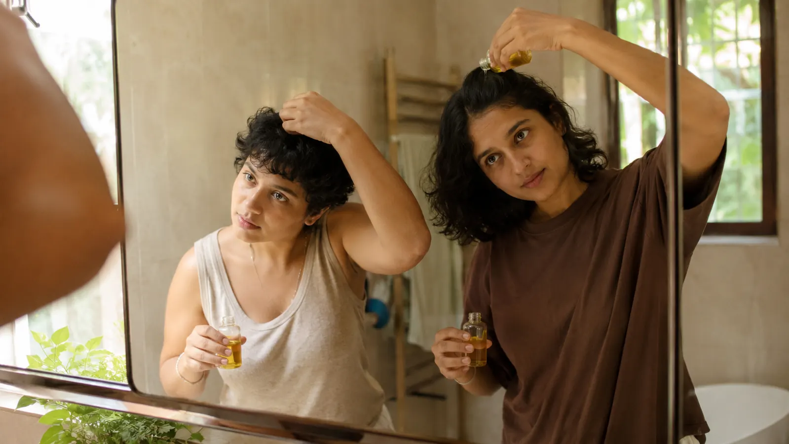 Couple standing at bathroom mirror, each applying a small amount of hair oil before their morning routine