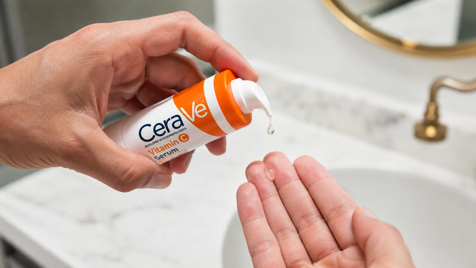 Person dispensing a few drops of vitamin C serum onto fingertips over a white bathroom sink