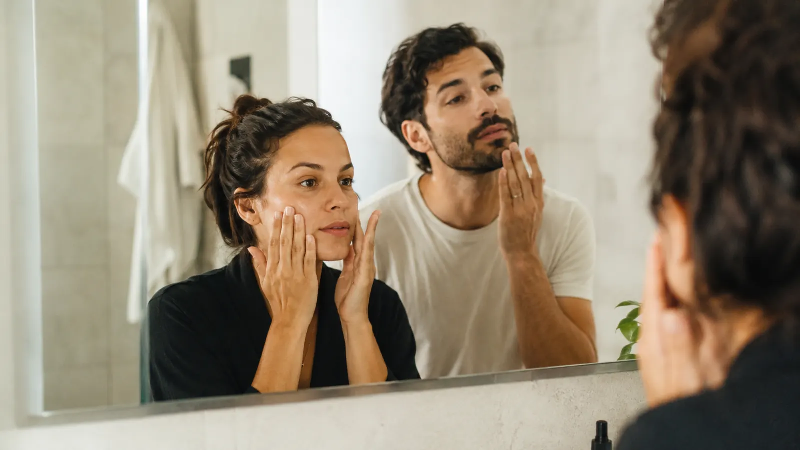 Couple doing their morning skincare routine side by side at a shared bathroom mirror