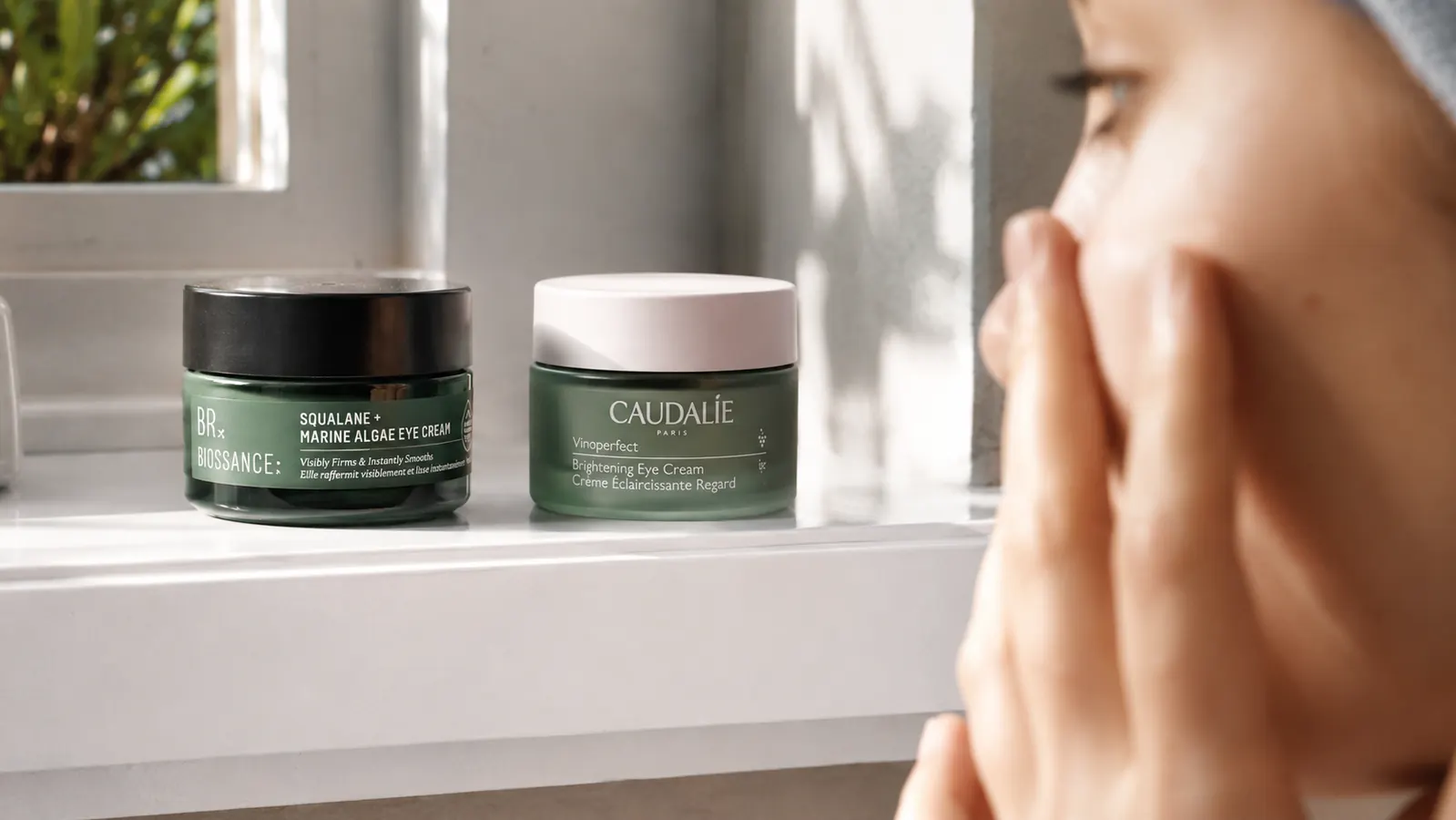 Two eye cream jars side by side on a white bathroom shelf with soft morning light