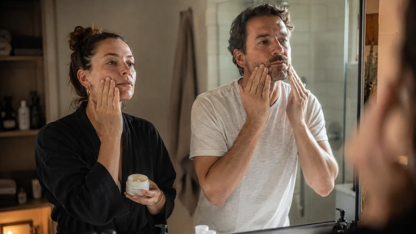 Couple doing morning skincare routines side by side at a bathroom mirror