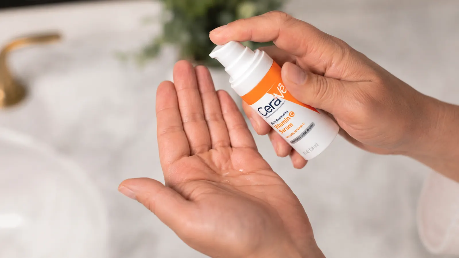 Close-up of the CeraVe Vitamin C Serum bottle being held with a pump depressed, thin clear serum visible