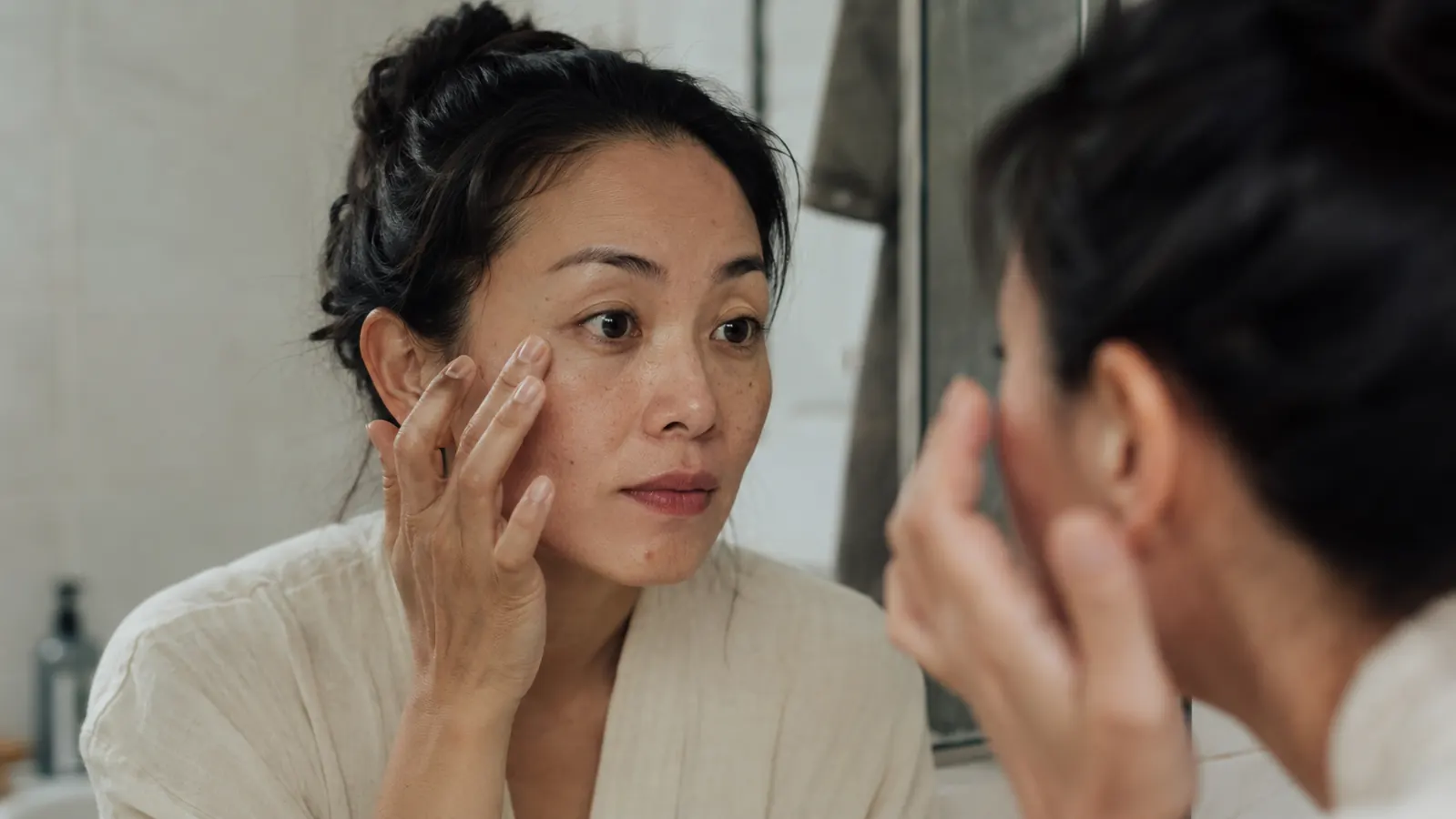 Person looking in bathroom mirror in morning light, examining under-eye area