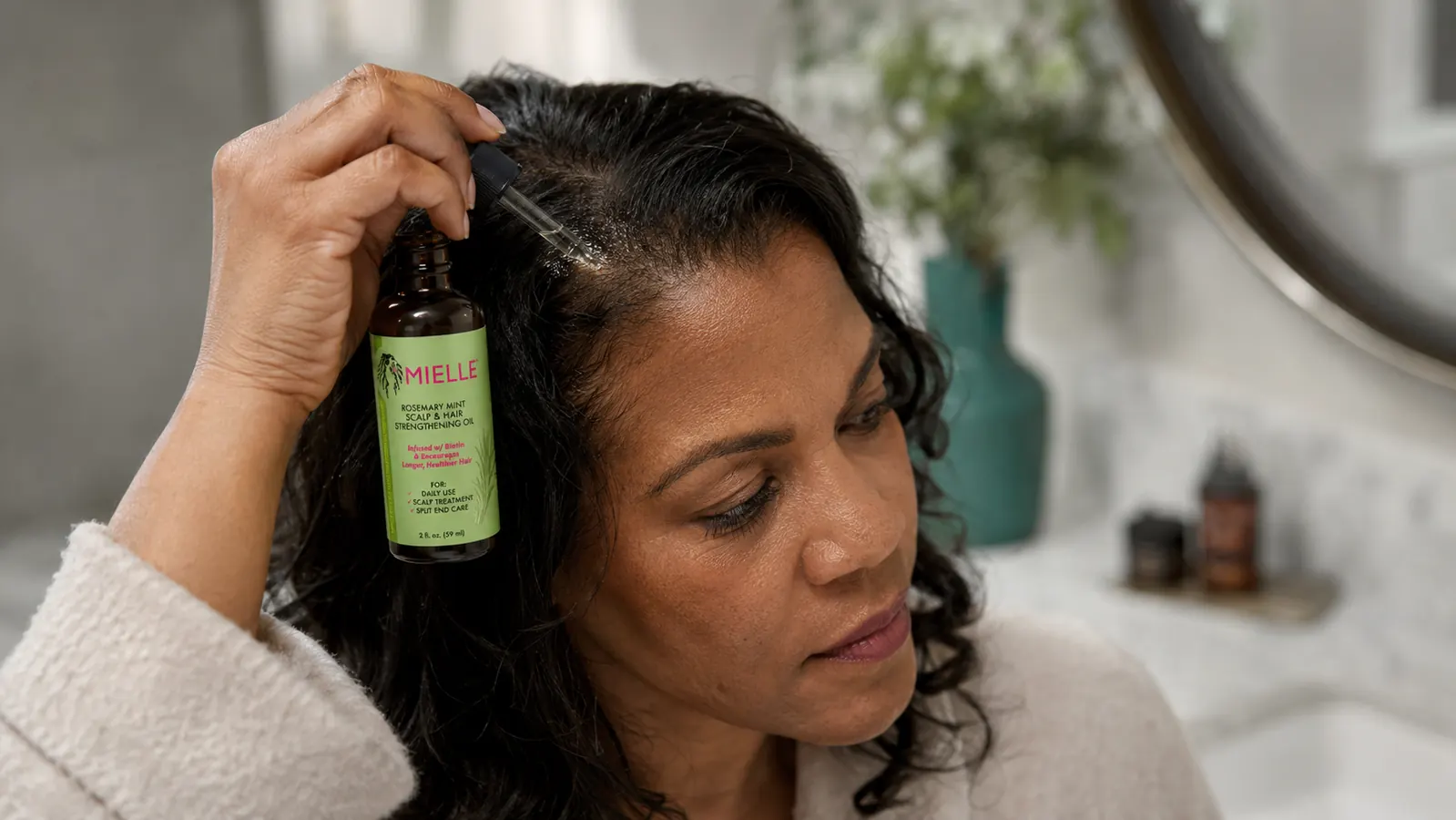 Bottle of Mielle Rosemary Mint Scalp Oil held in palm next to a small dropper, ready for use