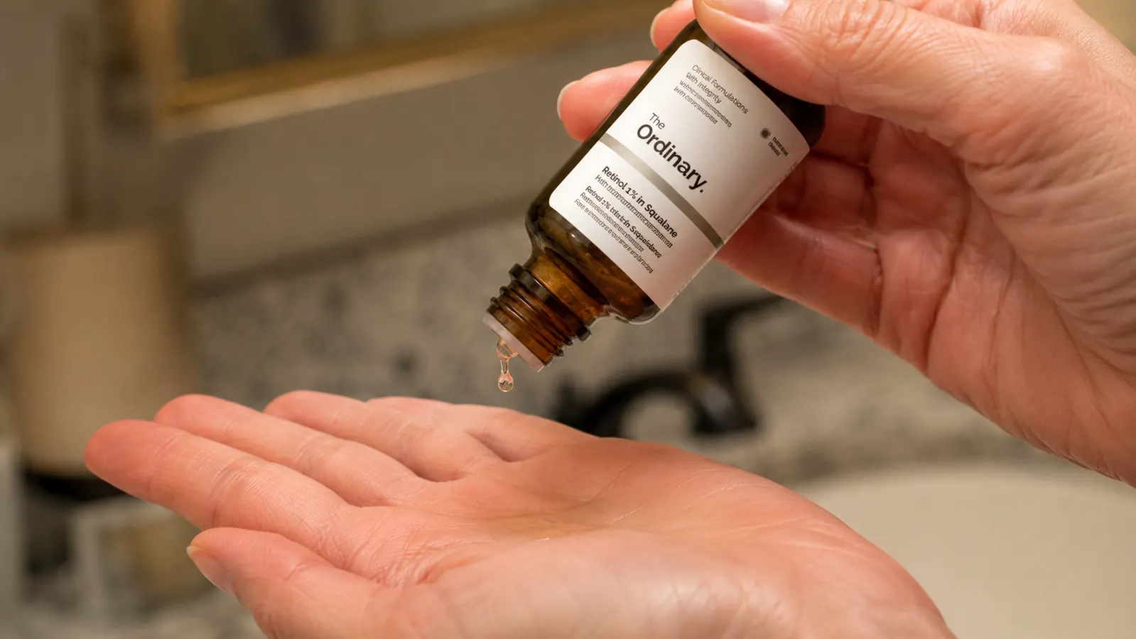 Hand holding a dropper bottle of The Ordinary Retinol 1% in Squalane above an open palm