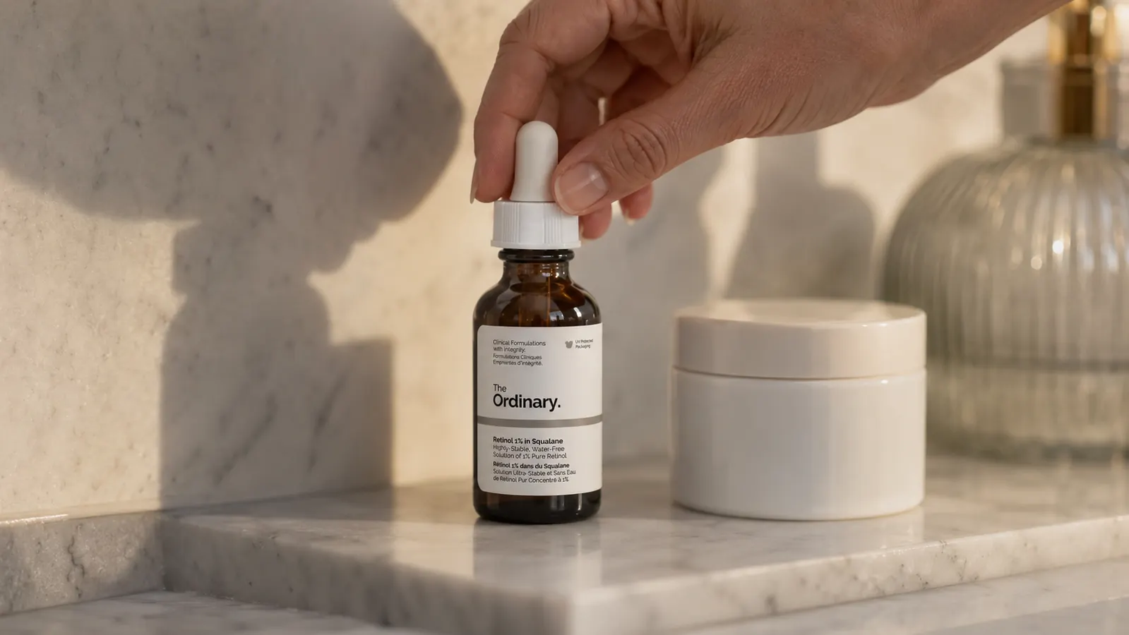 Small amber glass dropper bottle of retinol serum resting on a marble bathroom shelf next to a moisturizer