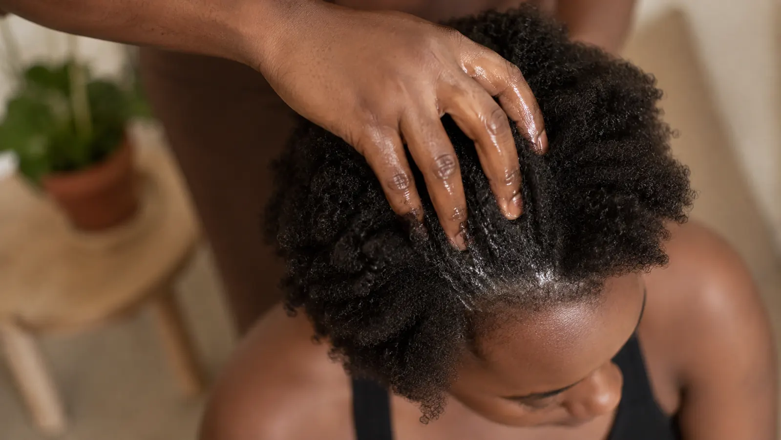 Overhead view of a hand applying oil to a scalp, fingers working through dark natural hair